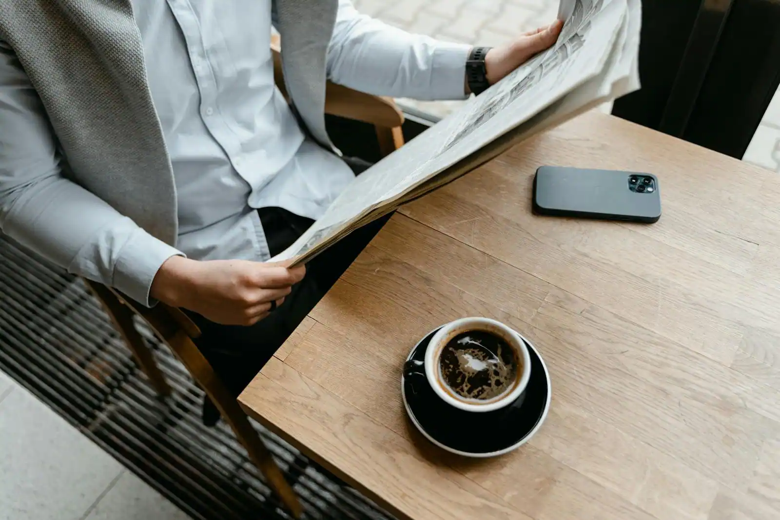 Smartphone affichant une application d'actualité économique anglophone à côté d'un journal papier et d'une tasse de café