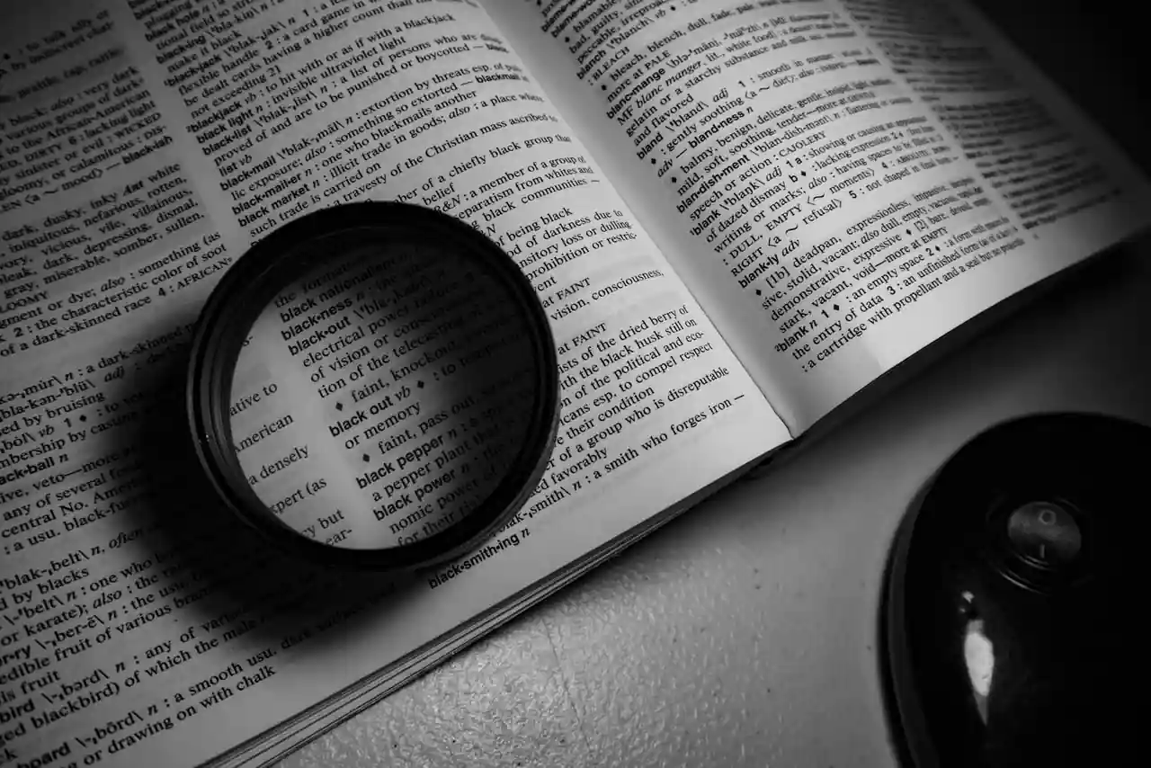 Dictionnaire ouvert et stylo posés sur une table, illustrant la recherche de synonymes et le choix des mots