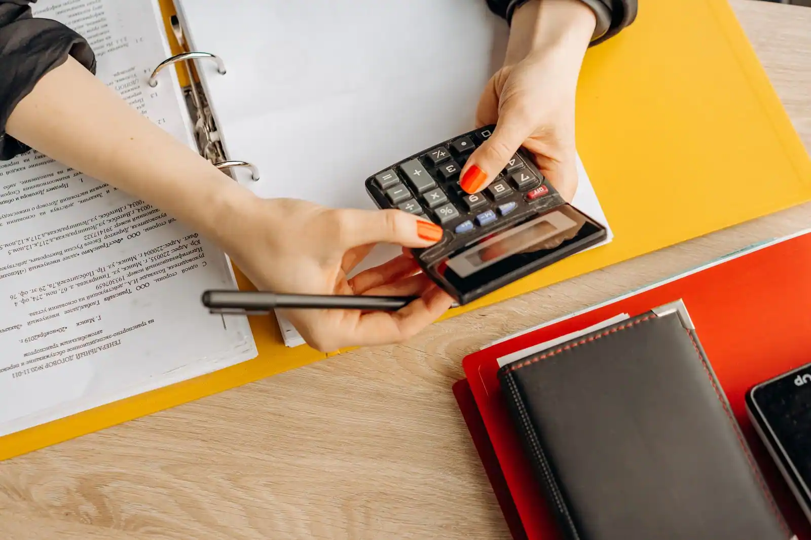 Bureau avec dossiers d'assurance, calculatrice et stylo posés sur une table en bois clair