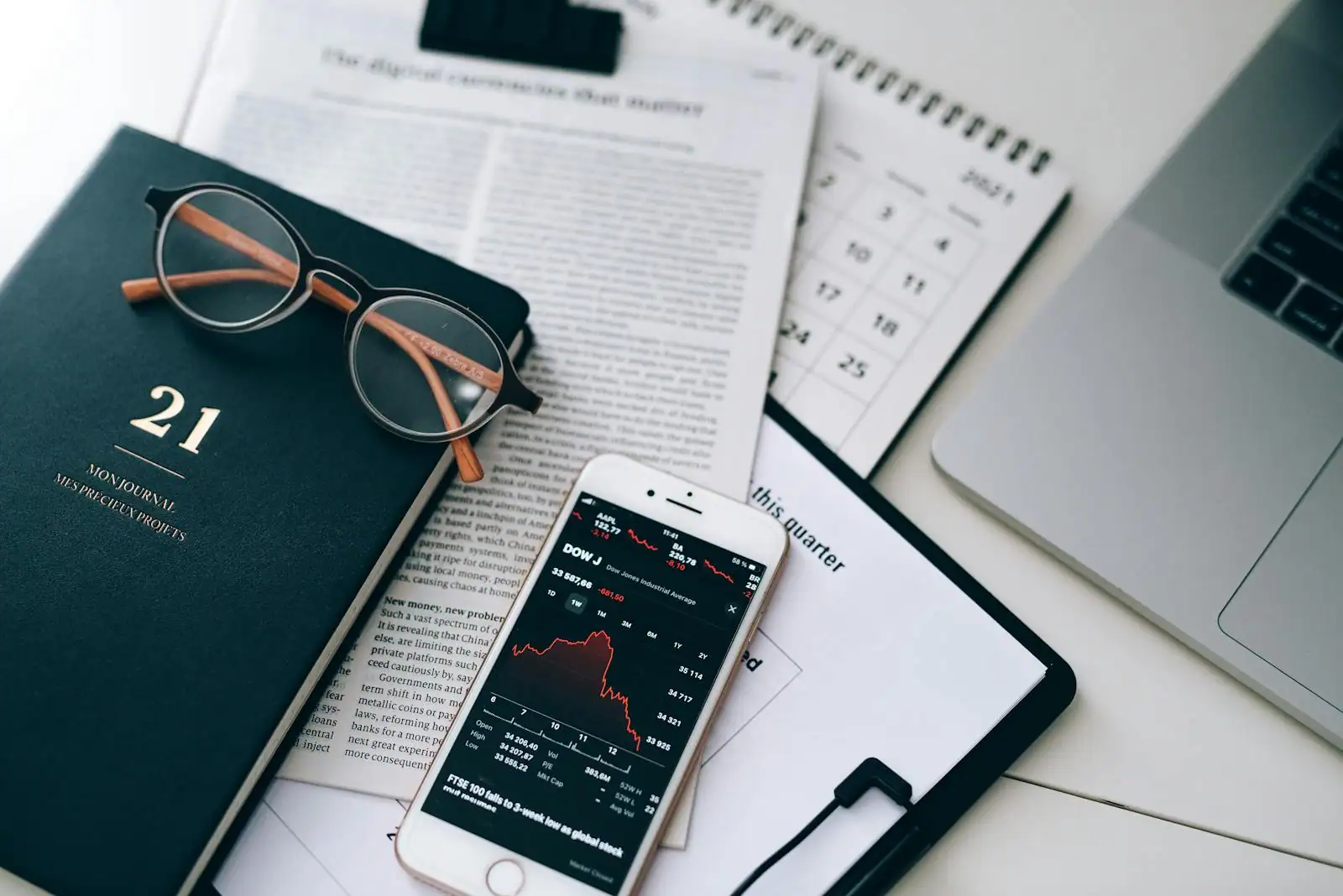 Bureau avec un journal économique ouvert, un ordinateur portable affichant un graphique et une tasse de café