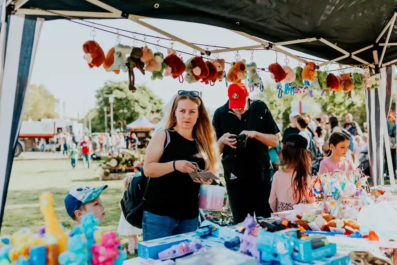 Étal de jouets en plein air avec peluches suspendues et visiteurs sur un marché