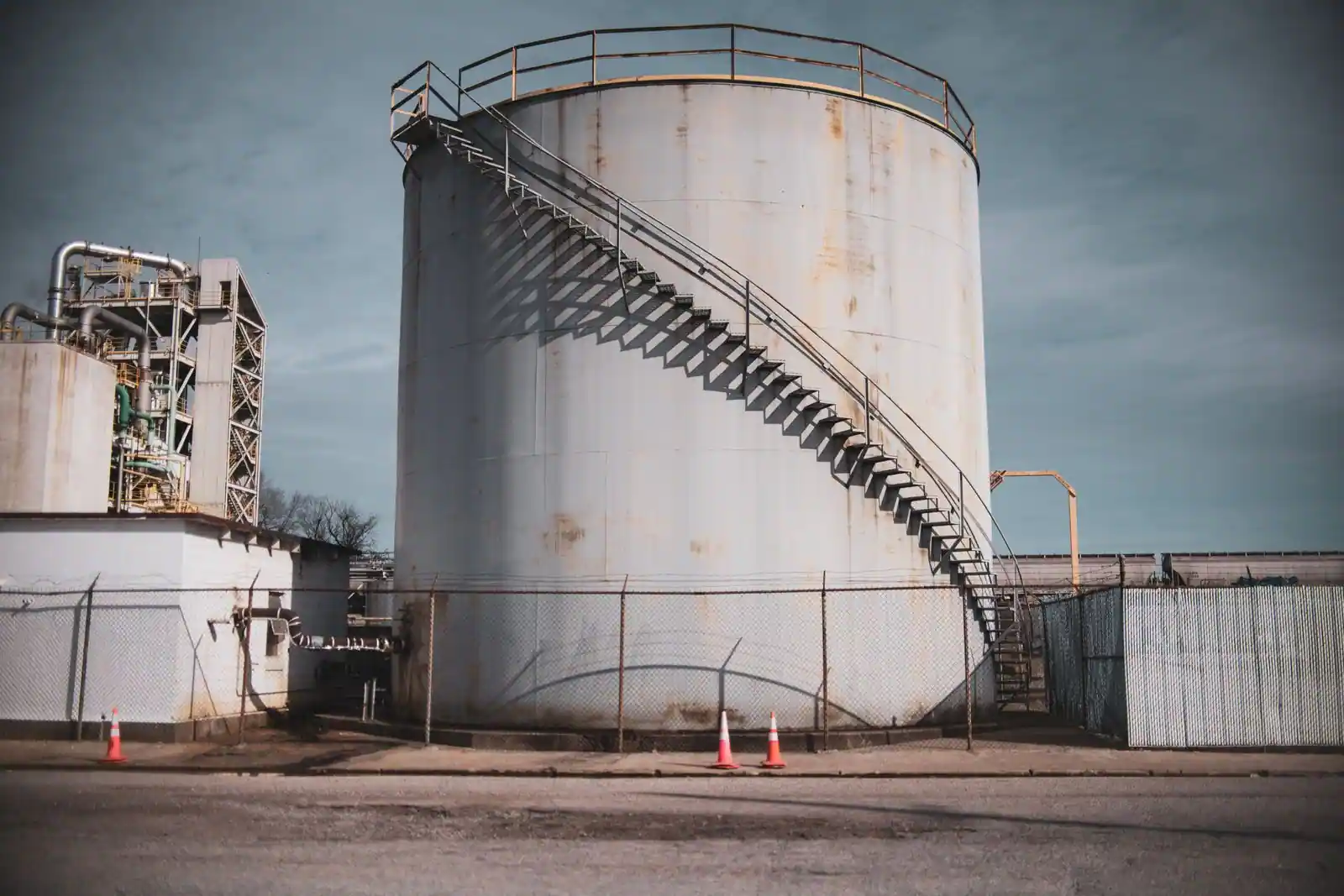 Grand réservoir de stockage industriel avec escalier extérieur et tuyauteries sur un site industriel