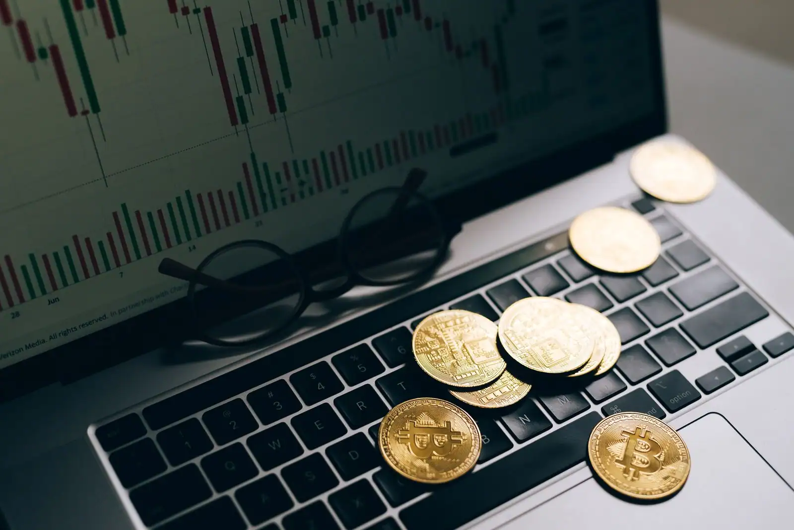 Des pièces de bitcoin posées sur le clavier d'un ordinateur portable affichant un graphique boursier en chandeliers.