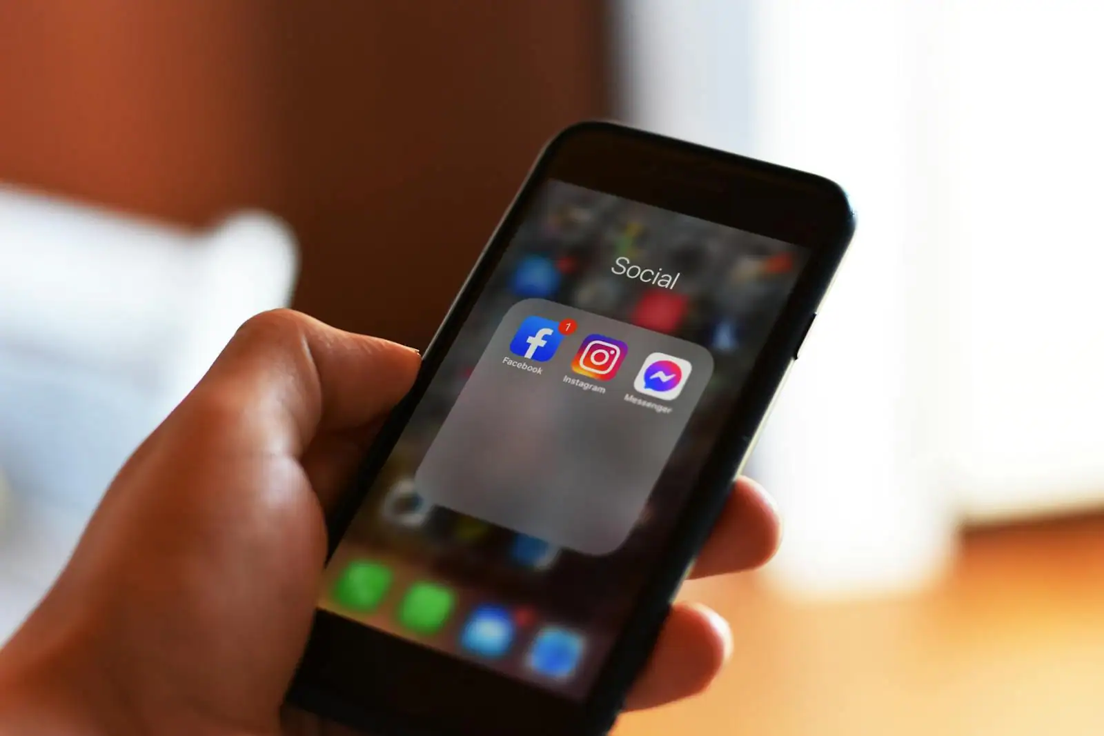 Main tenant un smartphone affichant des applications de réseaux sociaux (Facebook, Instagram, Messenger)