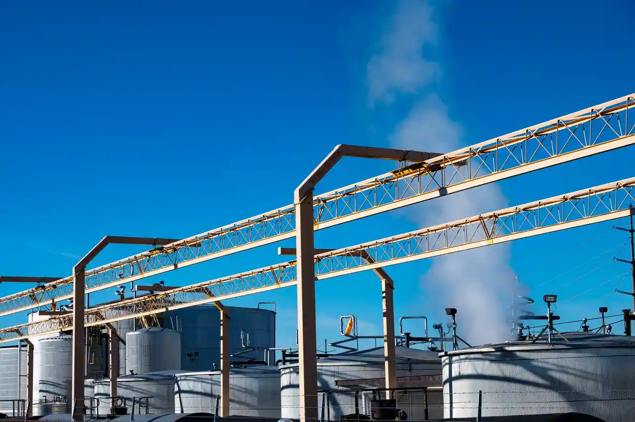 Cuves de stockage et structures métalliques d'un site industriel, panache de vapeur en arrière-plan.