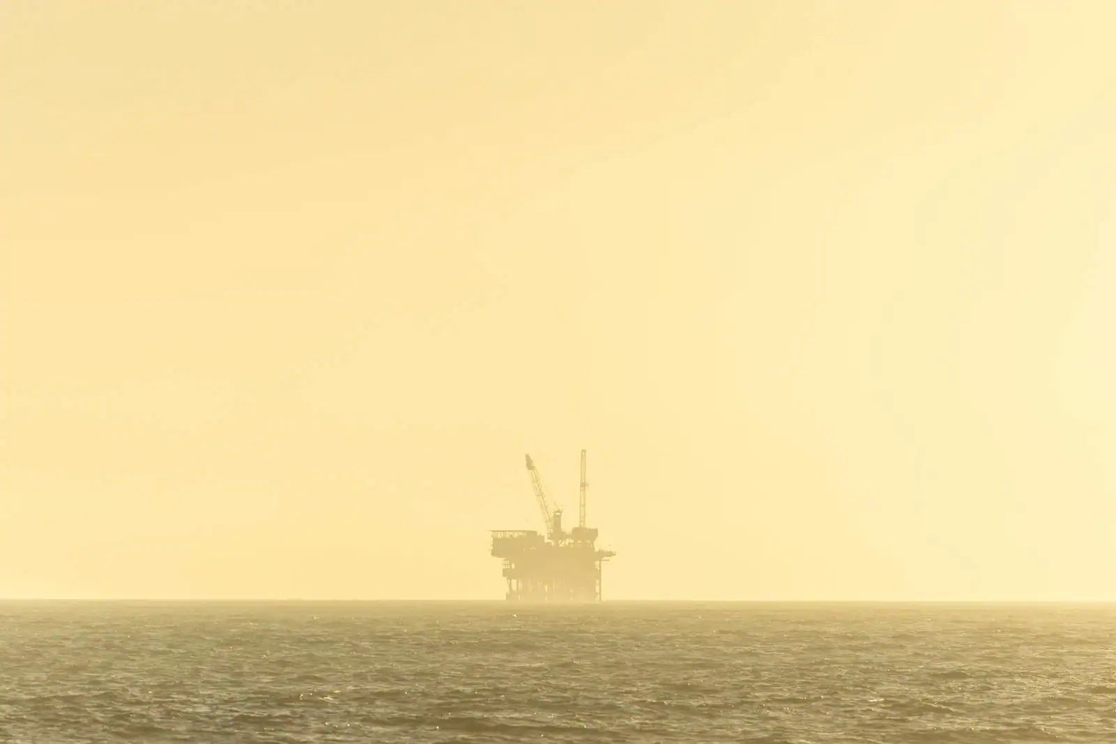 Plateforme pétrolière offshore à l'horizon sur la mer, ciel doré au couchant