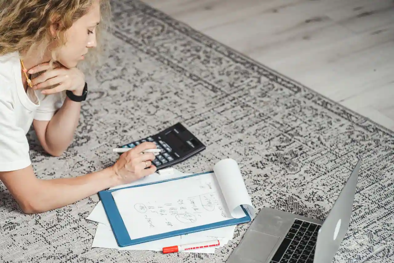 Calcul de revenus avec une calculatrice et des notes manuscrites, un ordinateur portable posé à côté