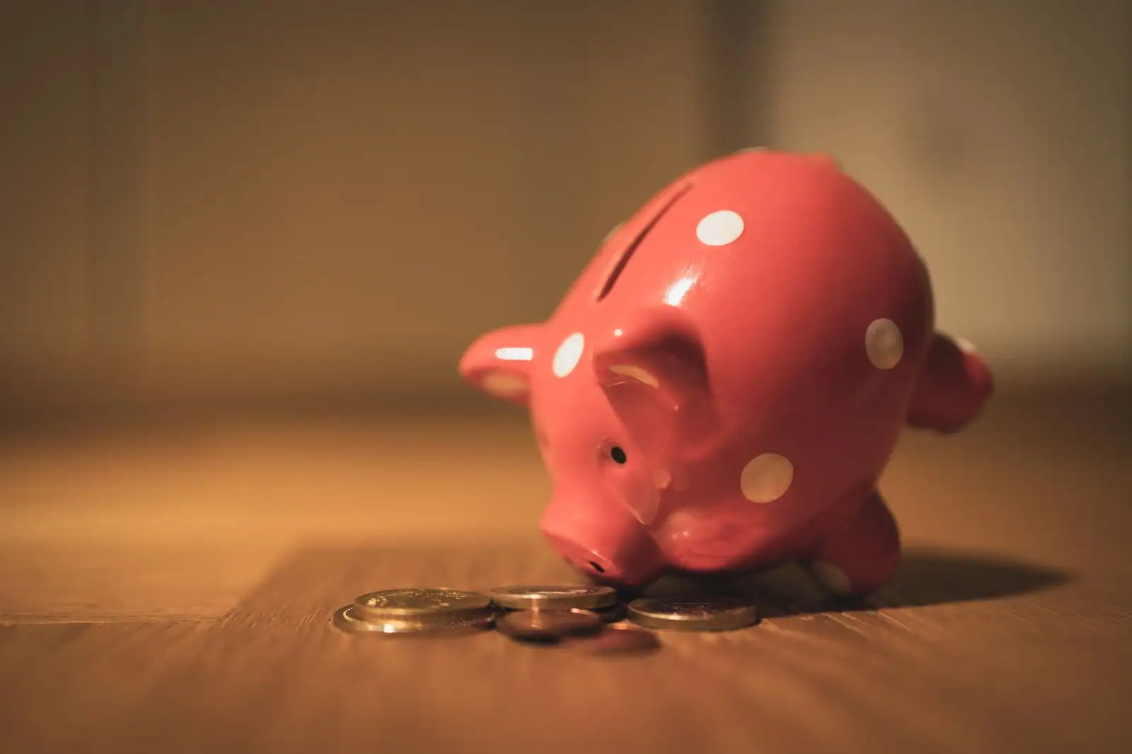 Tirelire rose posée près de quelques pièces de monnaie, évoquant l'épargne.
