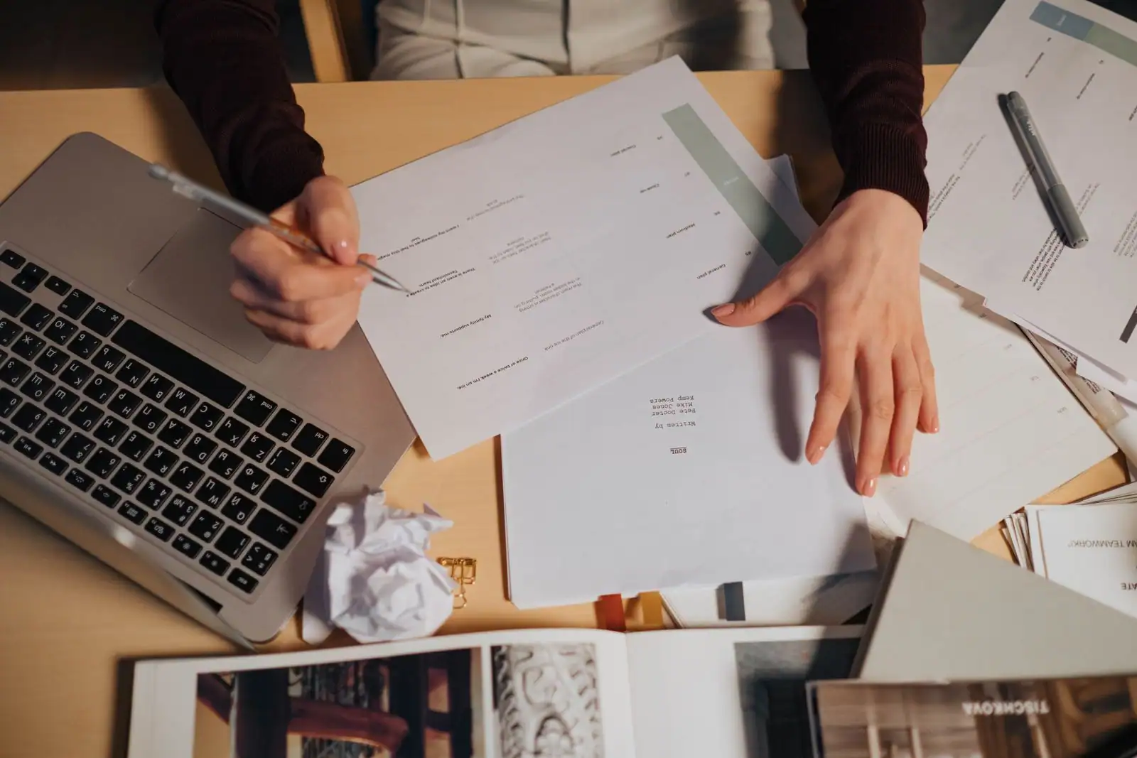 Mains à un bureau avec un ordinateur portable et des documents, en train de préparer une démarche.