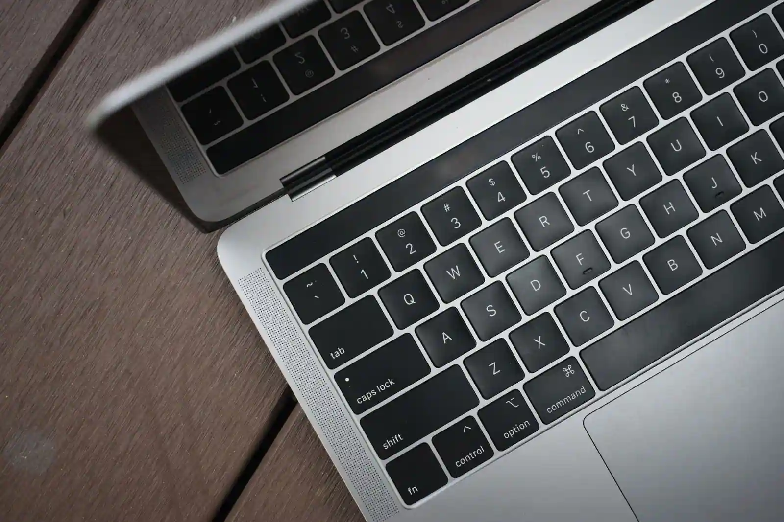 Le clavier argenté d'un ordinateur portable ouvert, posé sur une table en bois, vu de dessus.