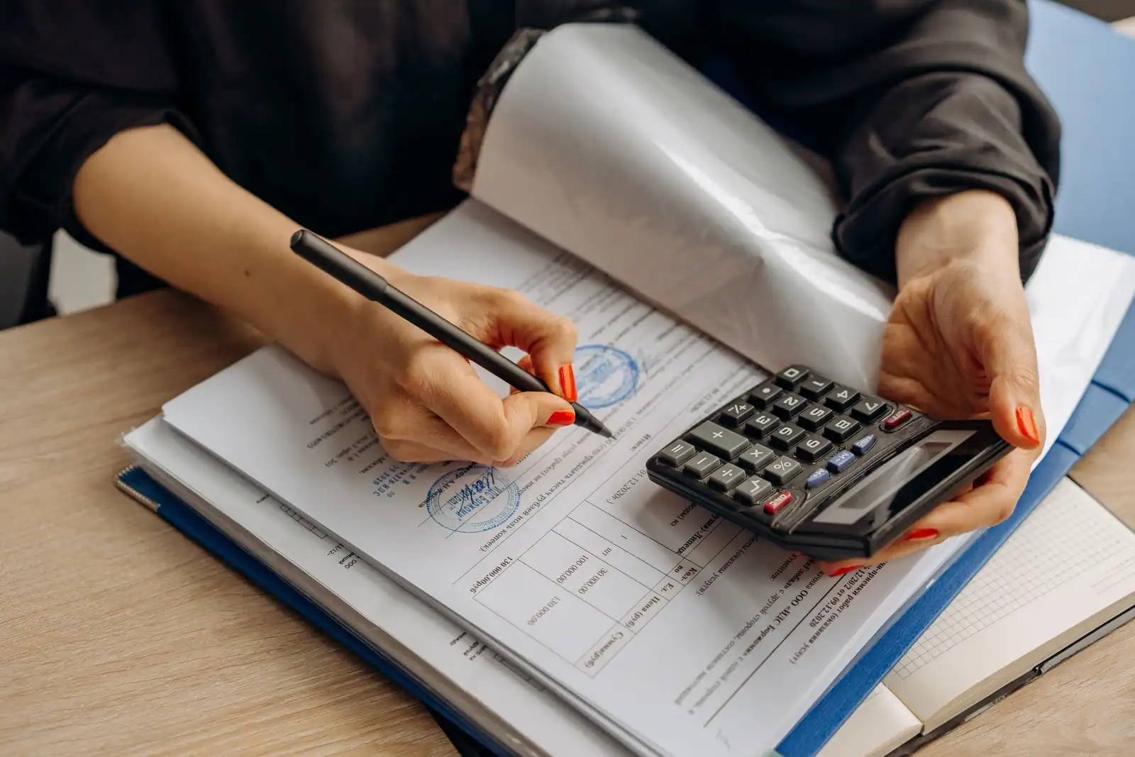 Personne examinant des documents administratifs avec une calculatrice et un stylo pour préparer ses impôts