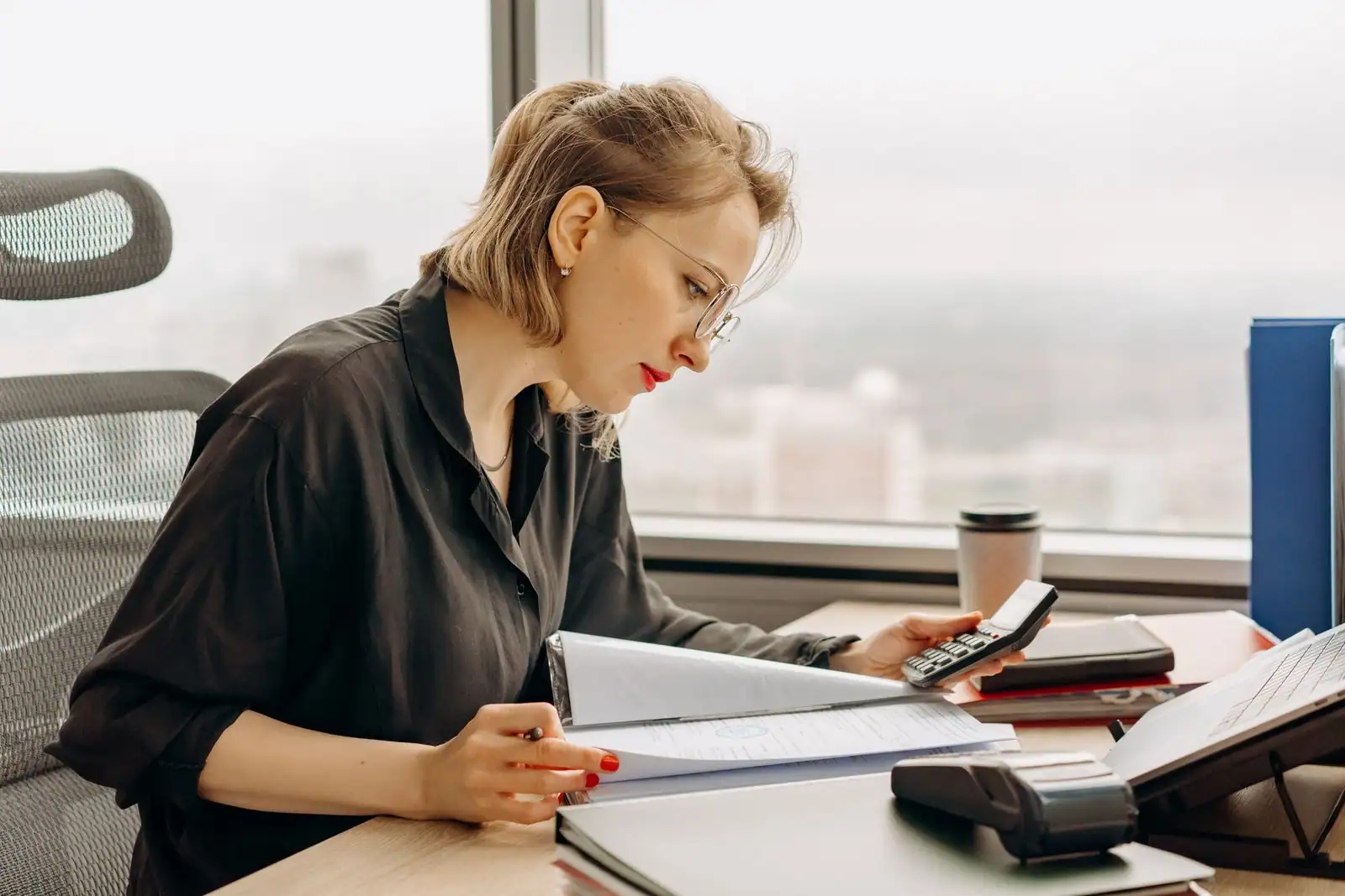 Professionnelle analysant des documents financiers avec une calculatrice sur un bureau.