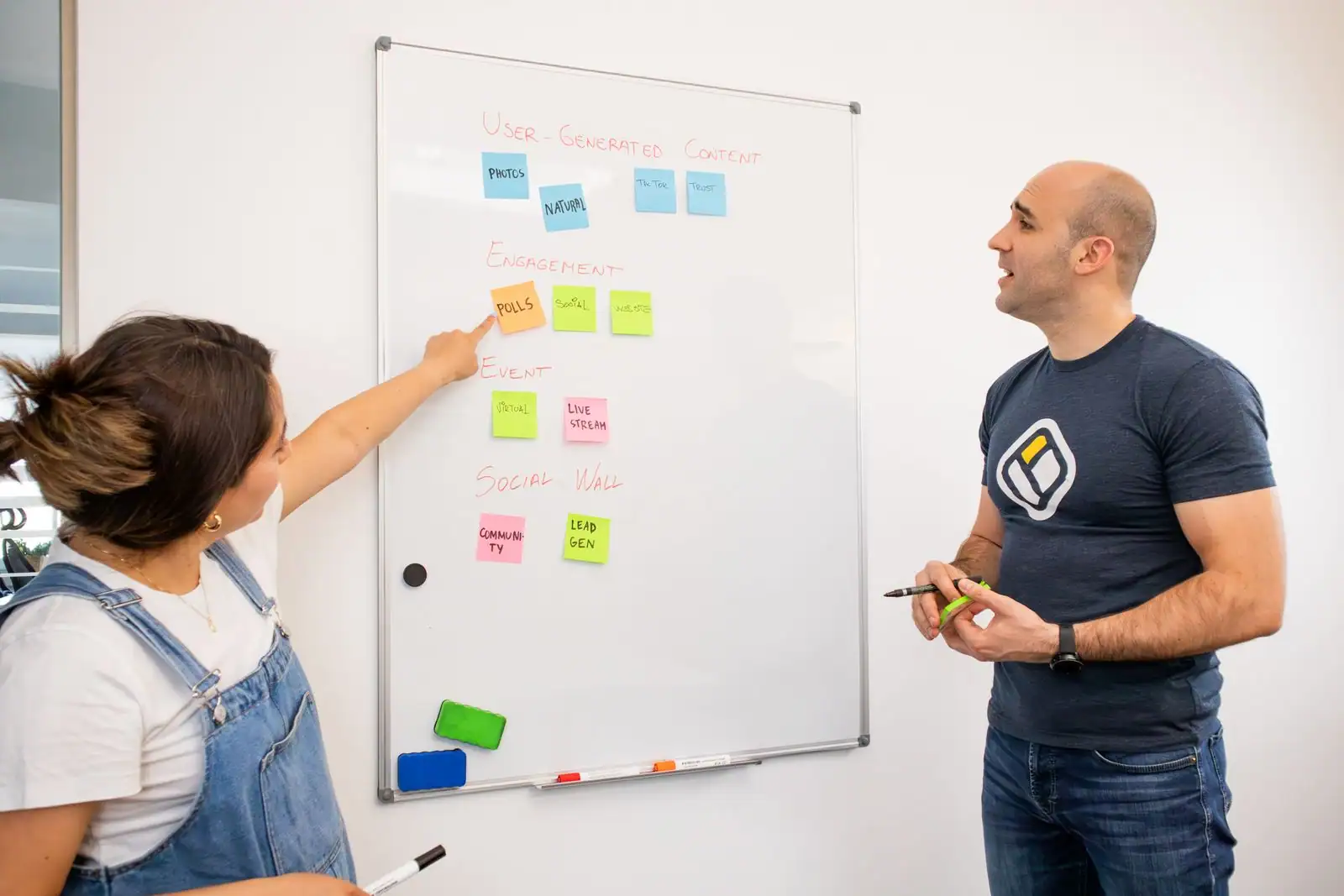 Deux personnes devant un tableau blanc couvert de notes colorées, en train de planifier une stratégie de communication.