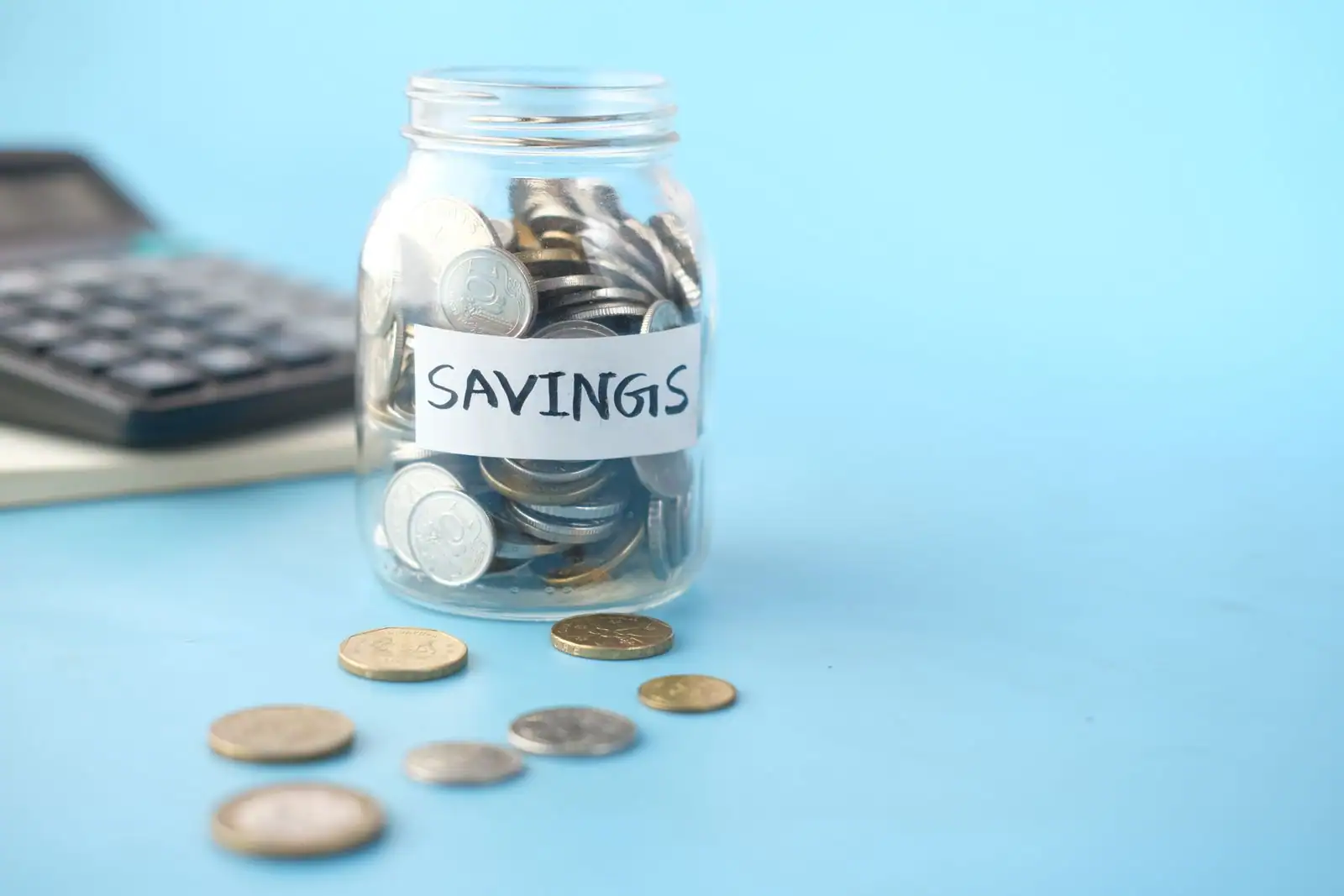 Bocal rempli de pièces de monnaie étiqueté « savings », posé près d'une calculatrice, illustrant l'épargne