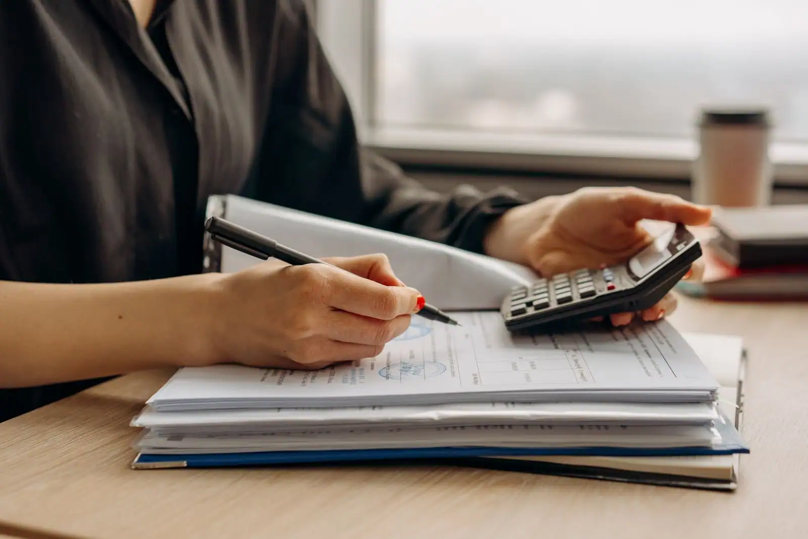 Personne utilisant une calculatrice au-dessus de documents financiers posés sur un bureau