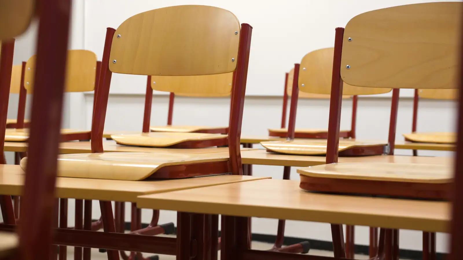 Salle de classe ordonnée, chaises de bois posées sur les pupitres, évoquant les métiers de l'école