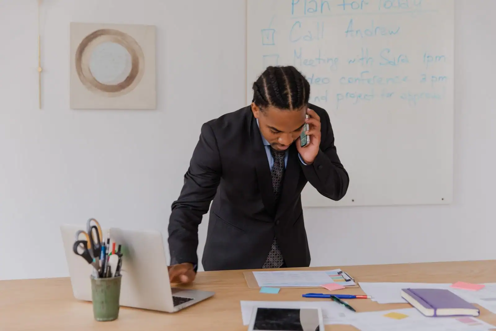 Homme d'affaires en costume au téléphone à son bureau, un ordinateur portable ouvert devant lui.
