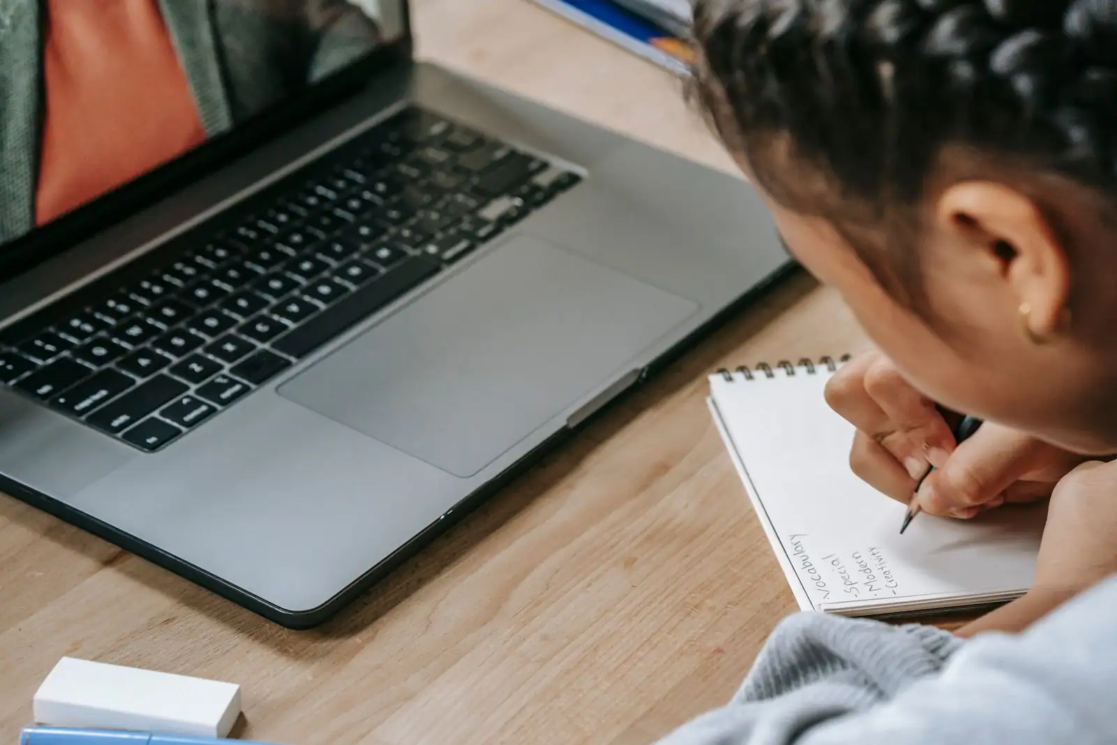 Personne adulte prenant des notes de vocabulaire dans un carnet à côté d'un ordinateur portable.