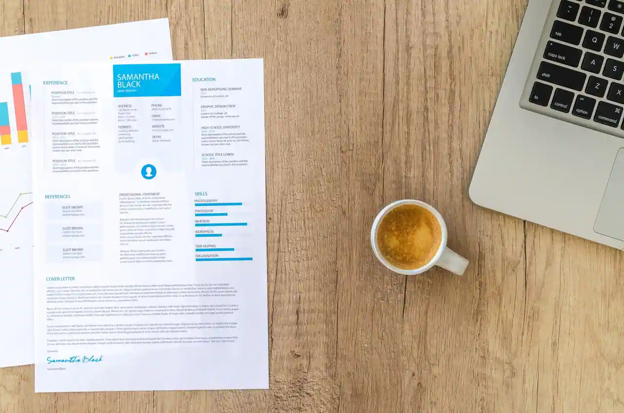 CV imprimé posé sur un bureau en bois, à côté d'un ordinateur portable et d'une tasse de café