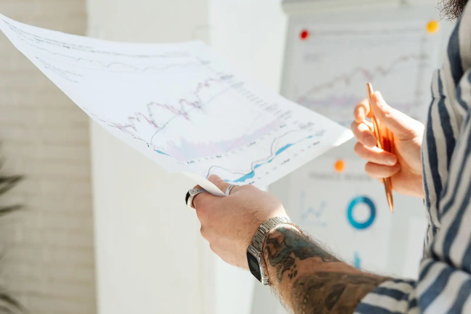 Personne analysant des graphiques financiers imprimés, stylo en main, devant des courbes de marché.