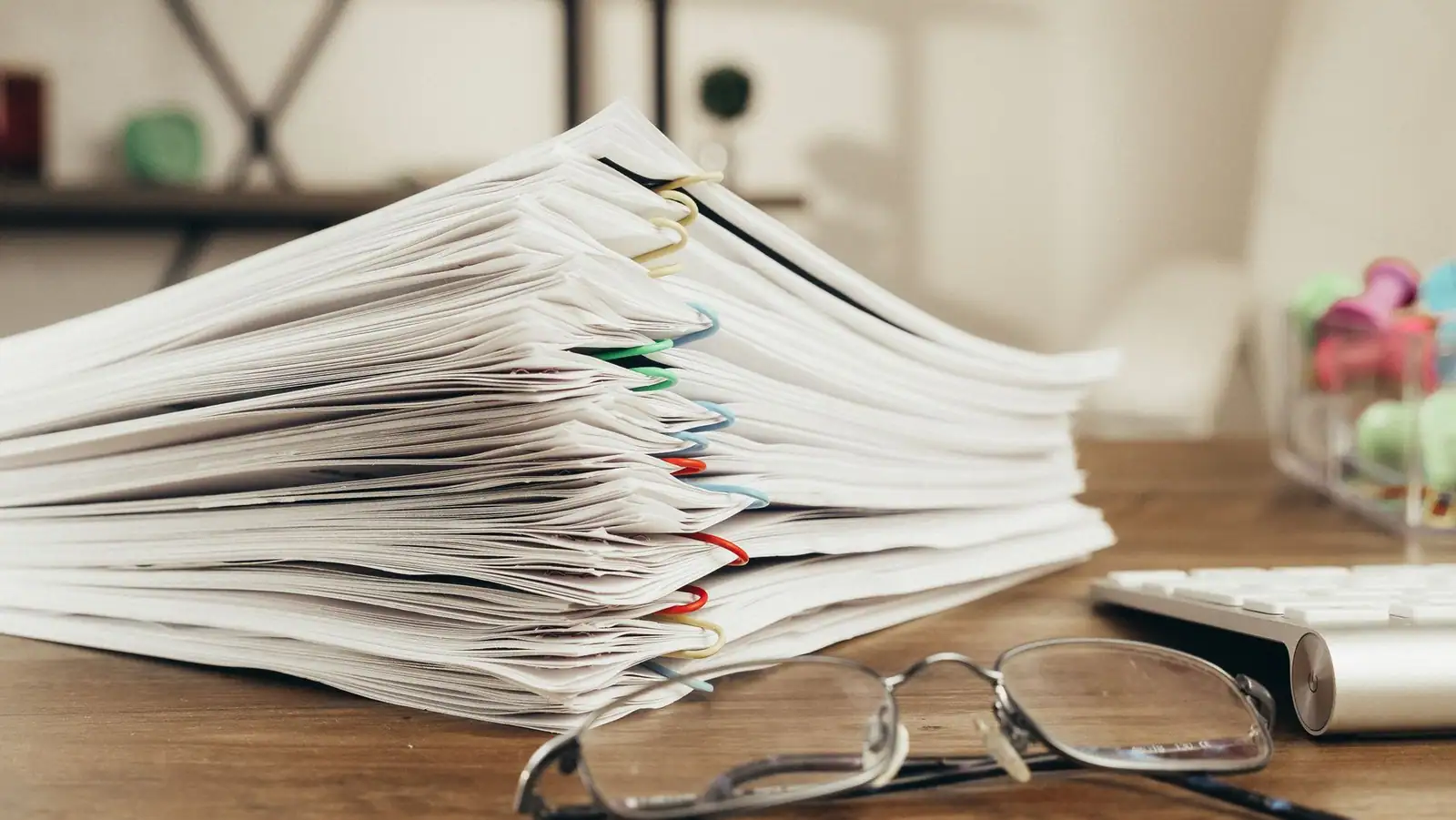 Épaisse liasse de documents retenus par des trombones sur un bureau, lunettes posées à côté