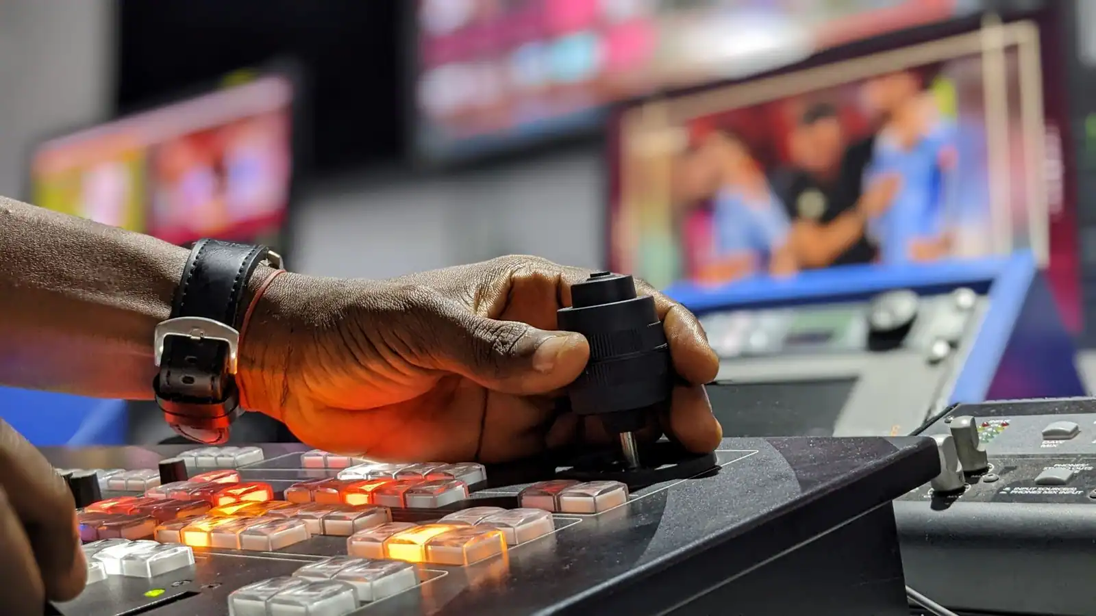 Main d’un technicien sur le mélangeur d’une régie de télévision, écrans de diffusion floutés en fond