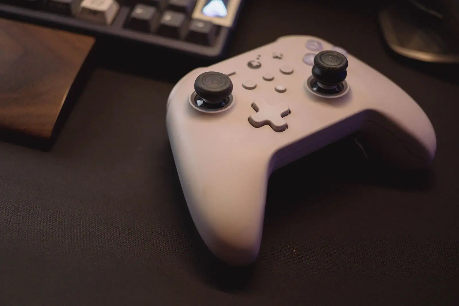 Manette de jeu vidéo blanche posée sur un bureau sombre, devant un clavier d’ordinateur rétroéclairé.