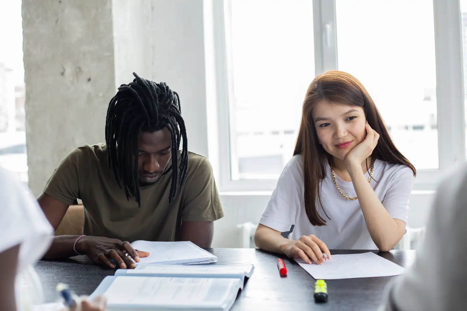 Deux étudiants installés à une table lumineuse travaillent sur des documents et des notes manuscrites.