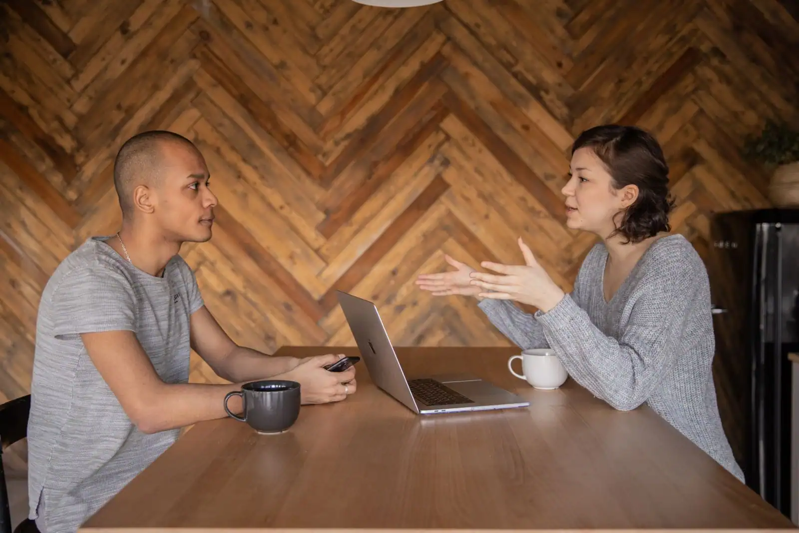 Deux personnes en conversation attentive, assises de part et d'autre d'une table en bois