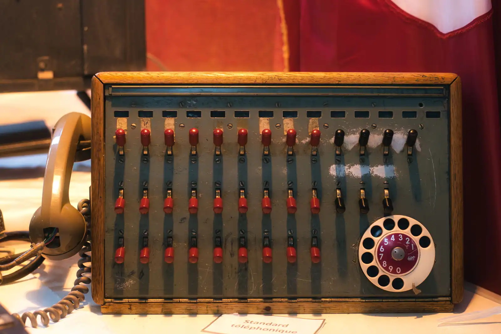Standard téléphonique ancien à commutateurs rouges et cadran rotatif, posé à côté d’un combiné.