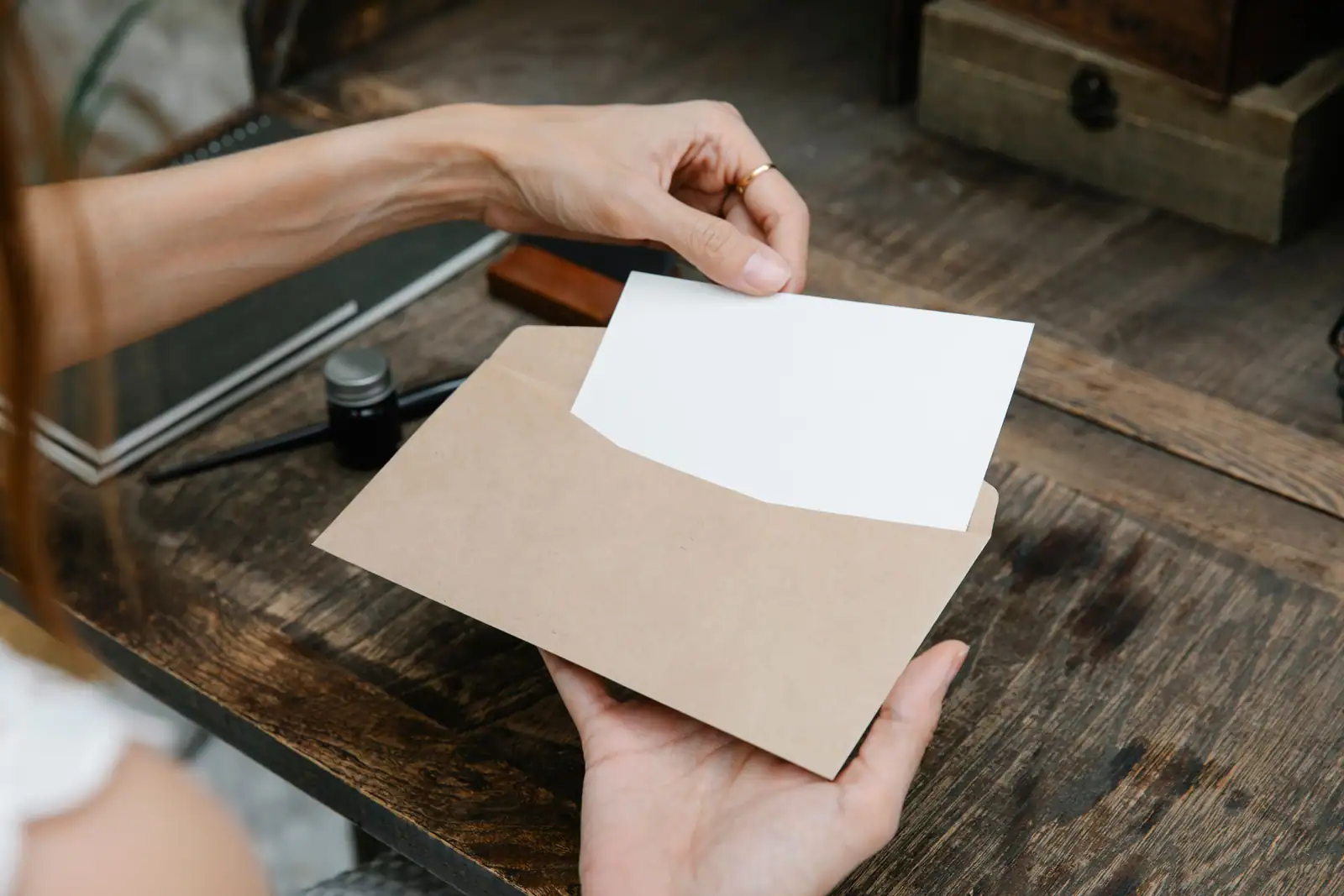 Une personne sort une feuille vierge d'une enveloppe kraft posée sur un bureau en bois