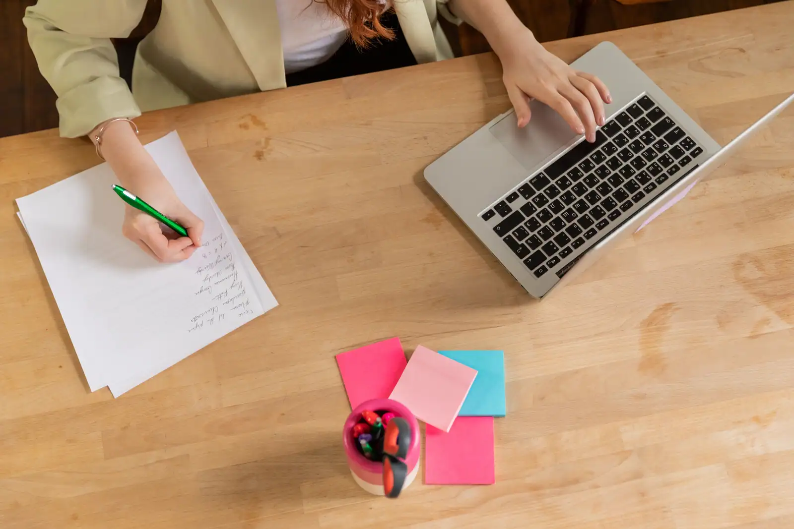 Vue de dessus d'un bureau : une personne prend des notes sur des feuilles et tape sur un ordinateur portable