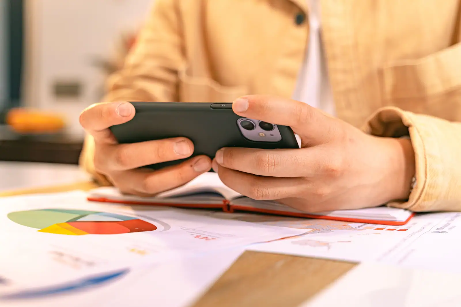 Mains tenant un téléphone au-dessus de documents chiffrés et de graphiques imprimés