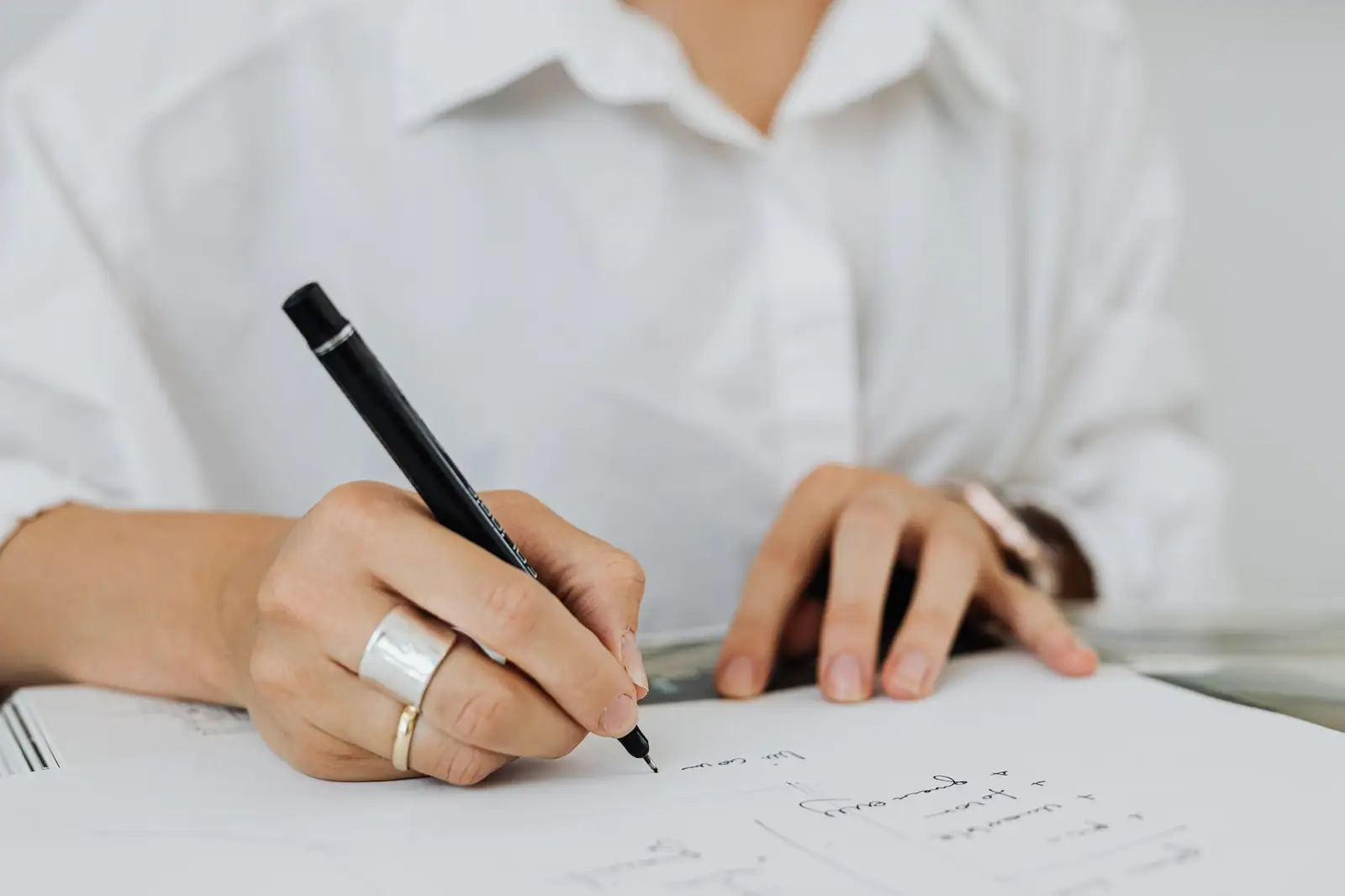 Personne en chemise claire écrivant à la main sur une feuille de papier posée sur un bureau lumineux