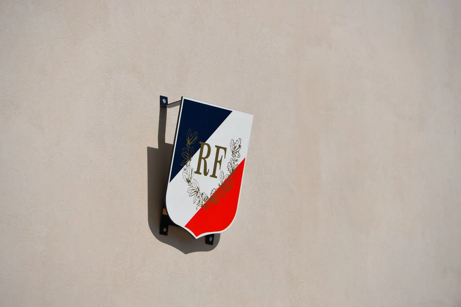 Écusson tricolore « RF » de la République française fixé sur le mur clair d'un bâtiment public